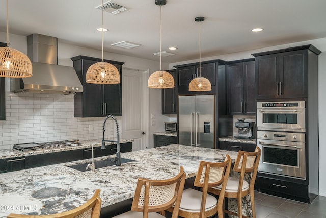 kitchen featuring sink, backsplash, hanging light fixtures, stainless steel appliances, and wall chimney range hood