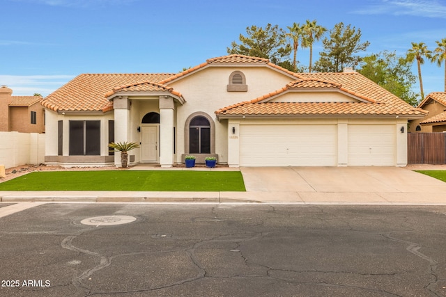 mediterranean / spanish home with a front lawn, a tile roof, fence, concrete driveway, and an attached garage