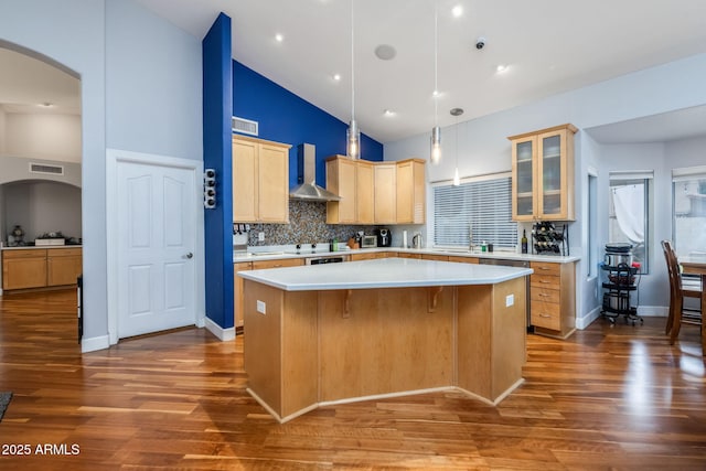 kitchen featuring visible vents, a kitchen island, arched walkways, light countertops, and wall chimney exhaust hood