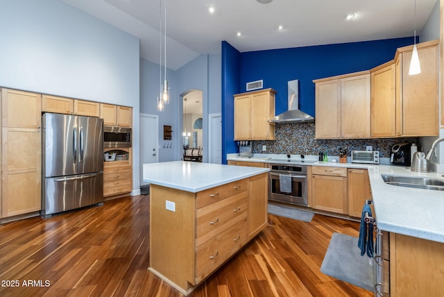 kitchen with arched walkways, a sink, appliances with stainless steel finishes, wall chimney range hood, and a center island