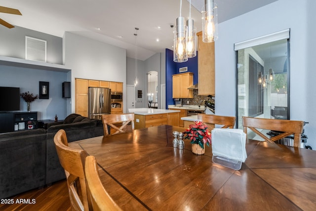 dining room with dark wood-style floors, ceiling fan with notable chandelier, and a towering ceiling