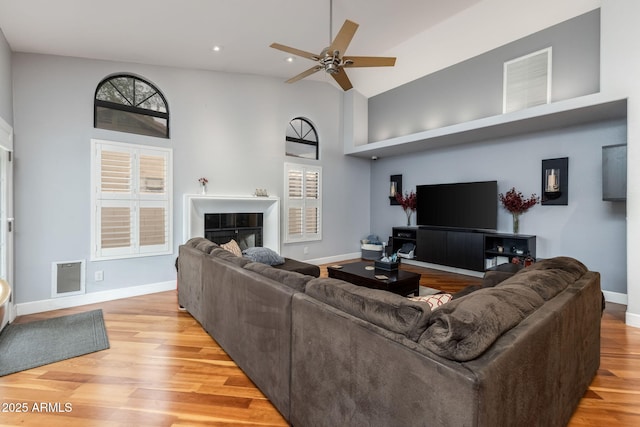 living room featuring ceiling fan, light wood-type flooring, baseboards, and a towering ceiling