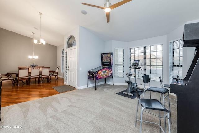 exercise room with carpet, wood finished floors, baseboards, lofted ceiling, and ceiling fan with notable chandelier