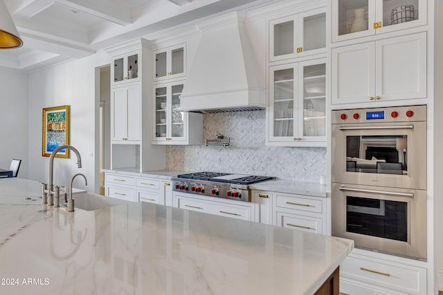 kitchen featuring custom range hood, light stone counters, appliances with stainless steel finishes, and white cabinetry