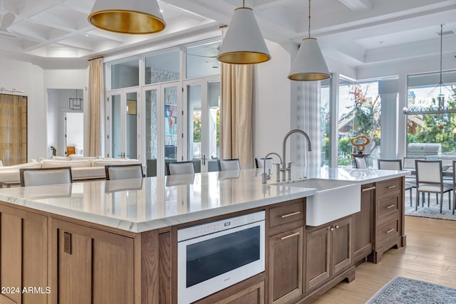 kitchen with a kitchen island with sink, light hardwood / wood-style flooring, sink, decorative light fixtures, and coffered ceiling