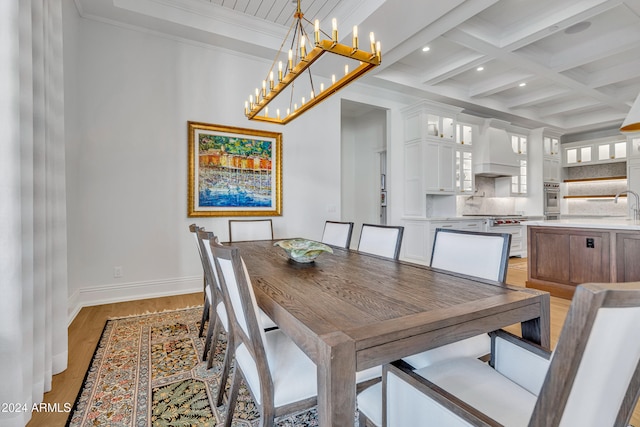 dining room with light wood-type flooring, beamed ceiling, crown molding, sink, and coffered ceiling