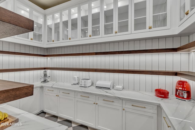 kitchen with wooden walls, white cabinetry, and light stone counters