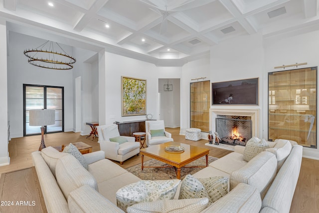 living room with a towering ceiling, beamed ceiling, coffered ceiling, and light wood-type flooring