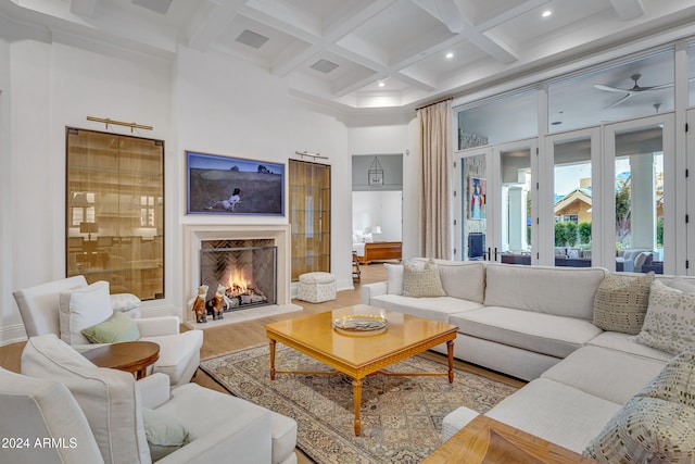 living room with coffered ceiling, beam ceiling, wood-type flooring, a premium fireplace, and a towering ceiling