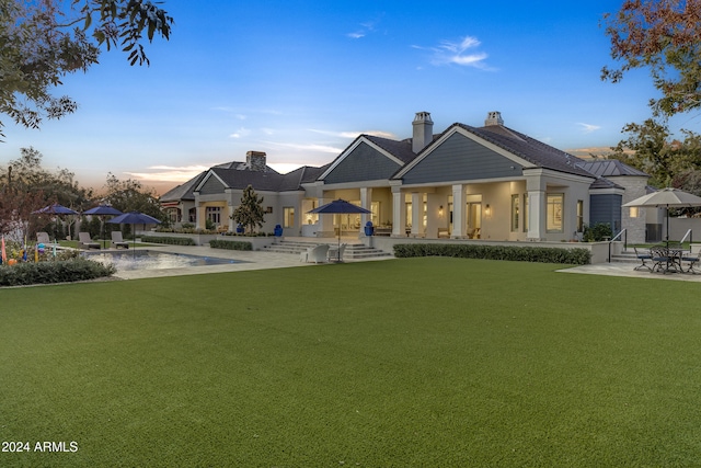 back house at dusk with a patio and a lawn