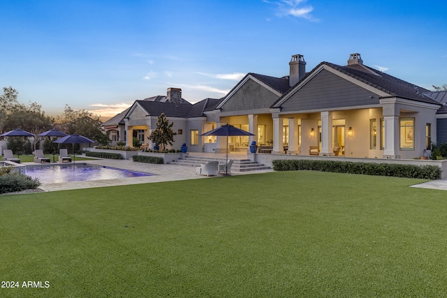 back house at dusk featuring a patio area and a lawn