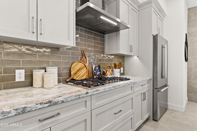 kitchen featuring white cabinets, appliances with stainless steel finishes, light stone countertops, and wall chimney range hood