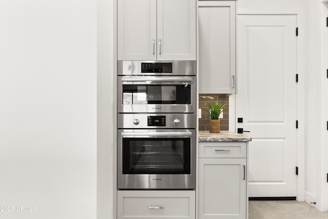 kitchen with light tile patterned flooring, tasteful backsplash, light stone counters, stainless steel double oven, and white cabinets