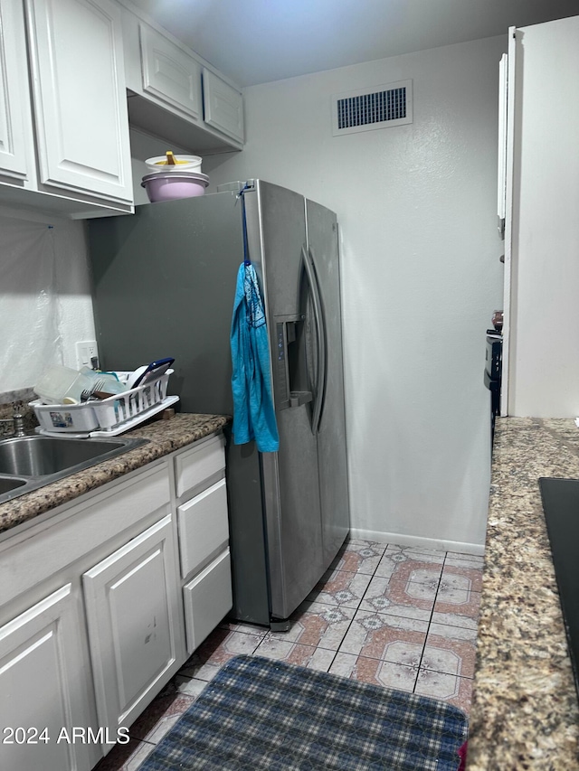 kitchen with dark stone counters, stainless steel fridge, white cabinetry, and sink