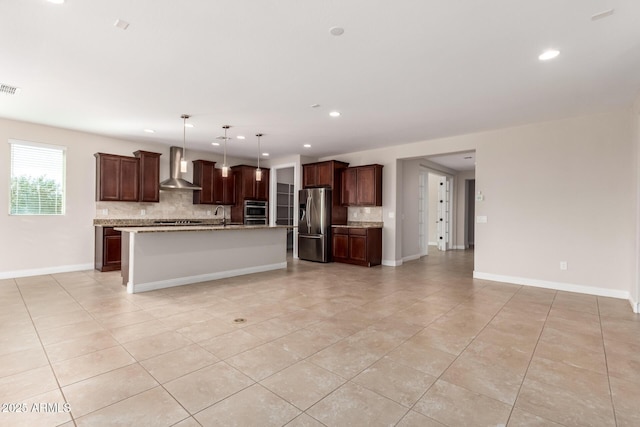 kitchen featuring wall chimney exhaust hood, tasteful backsplash, hanging light fixtures, a center island with sink, and stainless steel appliances