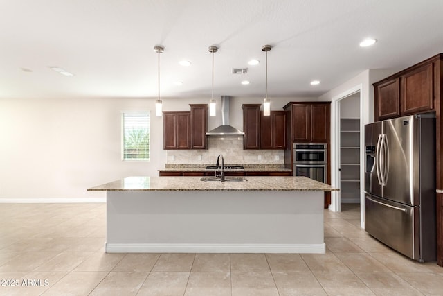 kitchen with wall chimney exhaust hood, stainless steel appliances, an island with sink, and hanging light fixtures