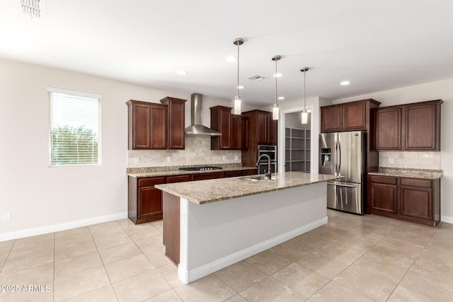 kitchen with sink, an island with sink, pendant lighting, stainless steel appliances, and wall chimney range hood