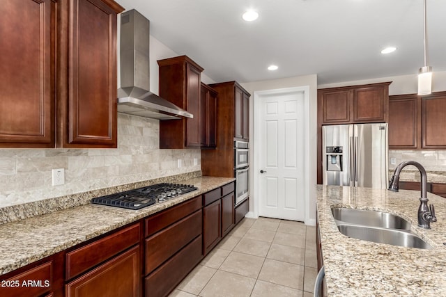 kitchen with pendant lighting, sink, appliances with stainless steel finishes, light stone counters, and wall chimney exhaust hood