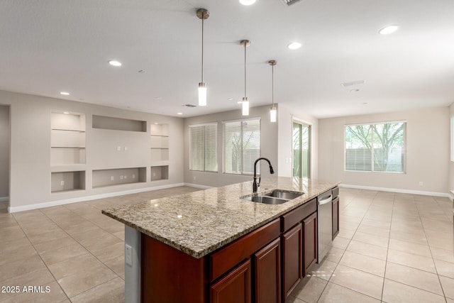 kitchen featuring built in features, decorative light fixtures, dishwasher, an island with sink, and sink