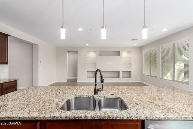 kitchen featuring pendant lighting, a kitchen island with sink, sink, and light stone counters