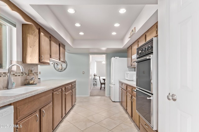 kitchen featuring light countertops, white appliances, backsplash, and a sink