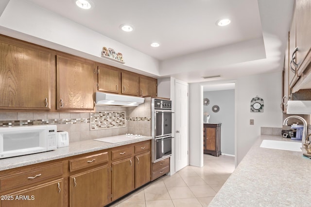 kitchen with light countertops, decorative backsplash, a sink, white appliances, and under cabinet range hood