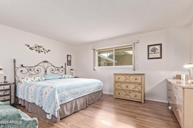 bedroom with light wood-style floors, baseboards, and a textured ceiling