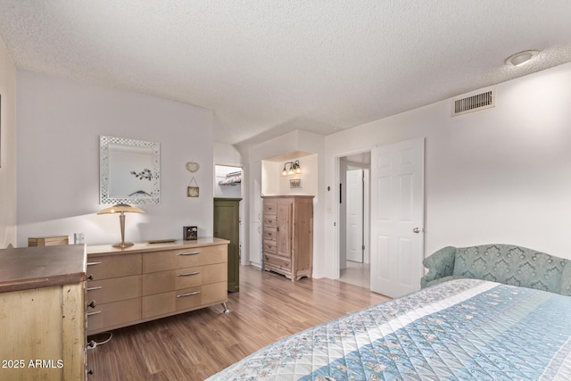 bedroom with a textured ceiling, visible vents, a walk in closet, and wood finished floors