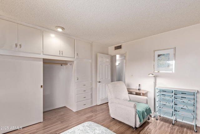 living area with a textured ceiling, light wood-style flooring, and visible vents