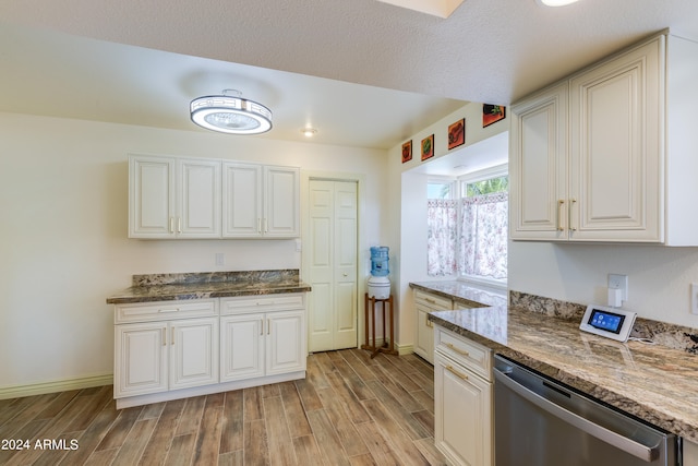 kitchen with stainless steel dishwasher, dark stone countertops, light hardwood / wood-style flooring, and white cabinets