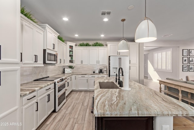 kitchen with hanging light fixtures, white appliances, light stone countertops, a kitchen island with sink, and white cabinets