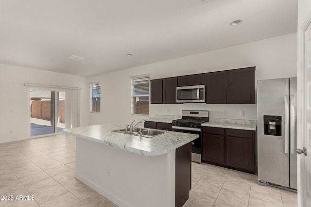 kitchen with sink, light tile patterned floors, dark brown cabinets, a center island with sink, and appliances with stainless steel finishes