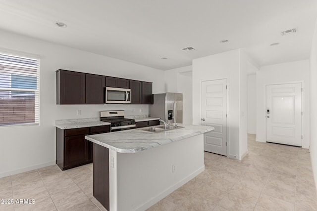 kitchen featuring sink, stainless steel appliances, an island with sink, light tile patterned floors, and dark brown cabinetry