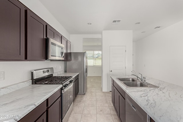 kitchen with light stone counters, sink, light tile patterned floors, appliances with stainless steel finishes, and dark brown cabinetry