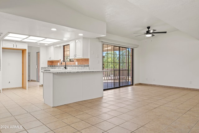 kitchen with backsplash, light stone countertops, white cabinets, and light tile patterned floors