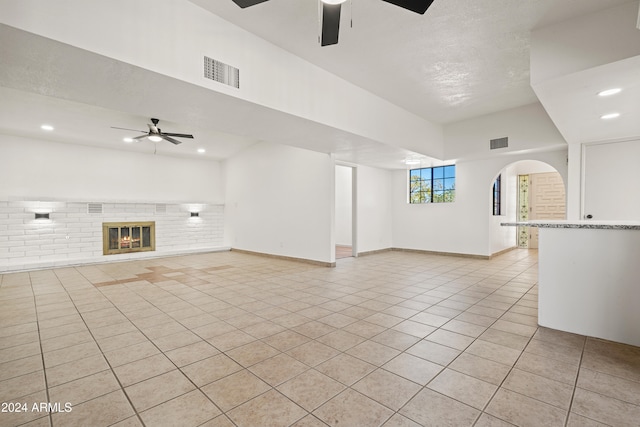 unfurnished living room featuring ceiling fan, light tile patterned floors, brick wall, and a textured ceiling