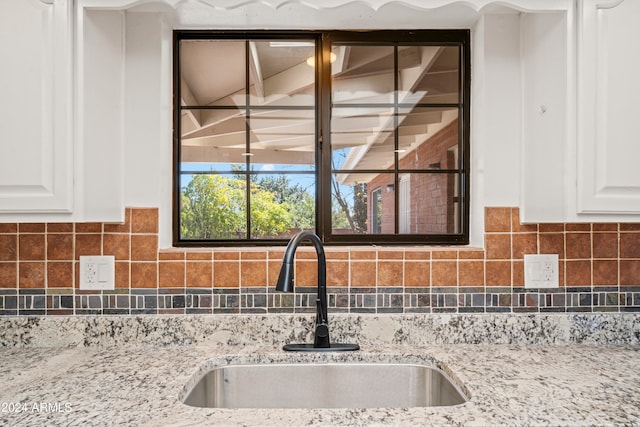 details with white cabinets, decorative backsplash, light stone countertops, and sink