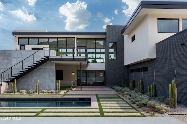 rear view of house with stucco siding, stairway, a patio area, brick siding, and an outdoor pool
