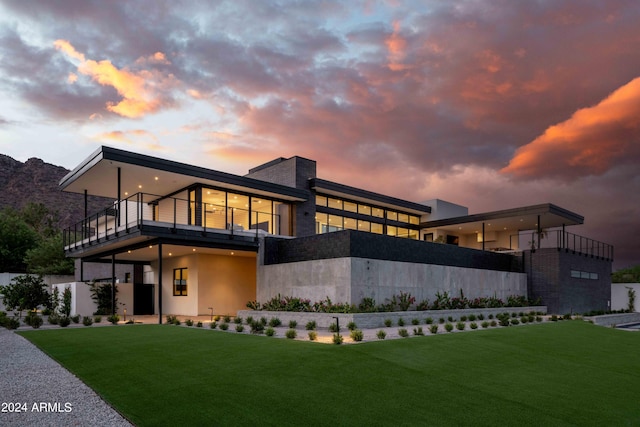 back of property at dusk with a yard and a balcony