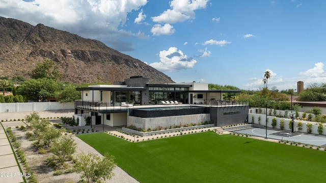 back of property with a mountain view, fence, and a lawn