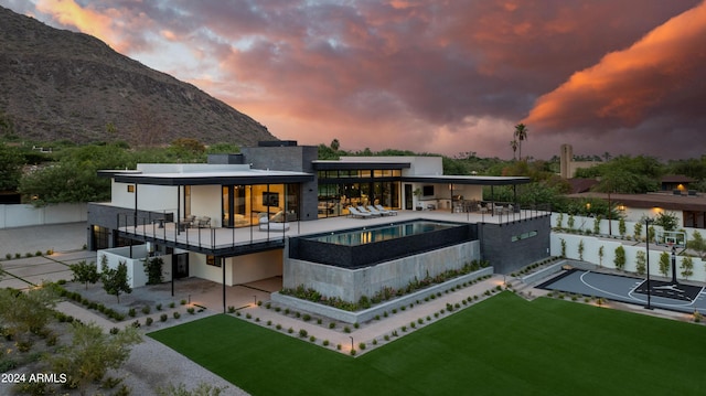 back of property at dusk with a mountain view, a patio area, a jacuzzi, a lawn, and community basketball court
