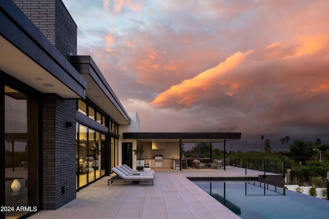pool at dusk featuring fence, a patio, an outdoor kitchen, and area for grilling