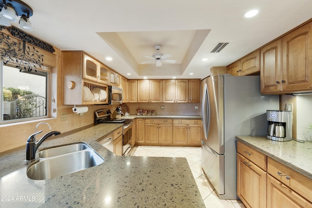 kitchen with light stone countertops, appliances with stainless steel finishes, a tray ceiling, ceiling fan, and sink