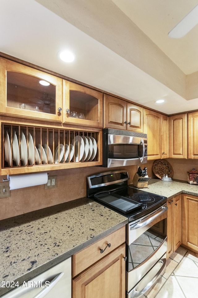 kitchen with appliances with stainless steel finishes, light stone counters, and light tile patterned flooring