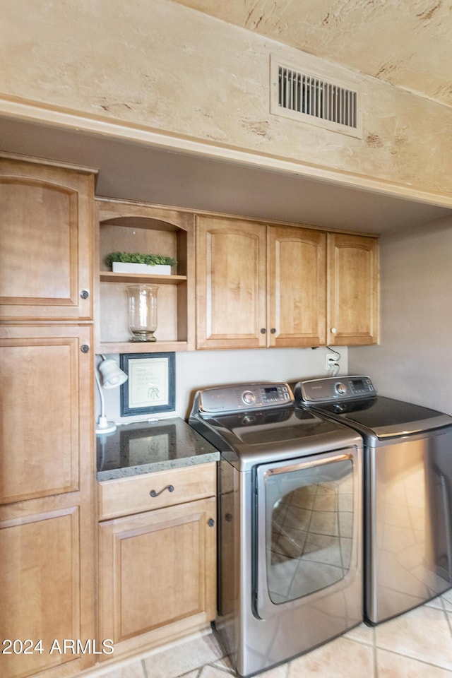 clothes washing area featuring cabinets, light tile patterned flooring, and washing machine and dryer