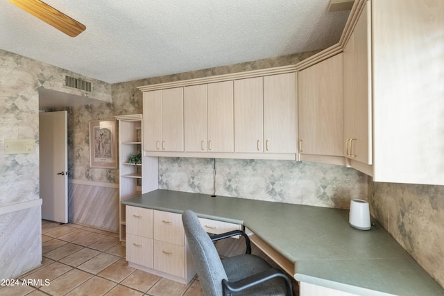 unfurnished office featuring ceiling fan, light tile patterned floors, built in desk, and a textured ceiling