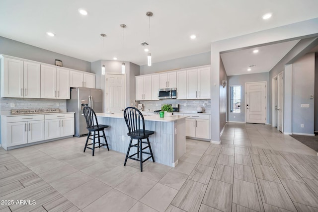 kitchen with pendant lighting, stainless steel appliances, light countertops, white cabinets, and an island with sink