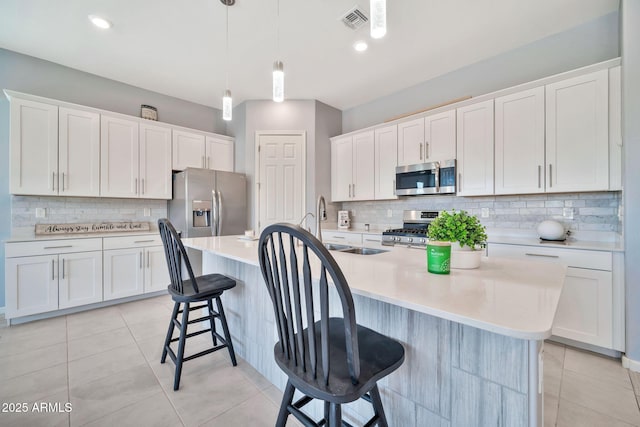 kitchen featuring appliances with stainless steel finishes, light countertops, white cabinetry, and a kitchen island with sink