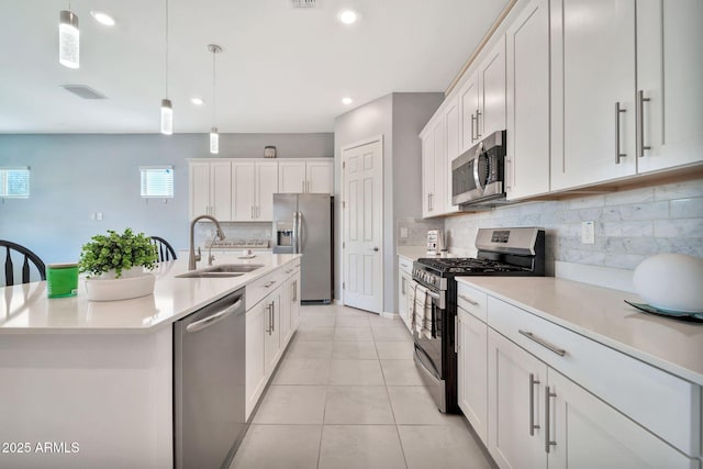 kitchen featuring a center island with sink, white cabinets, decorative light fixtures, stainless steel appliances, and light countertops