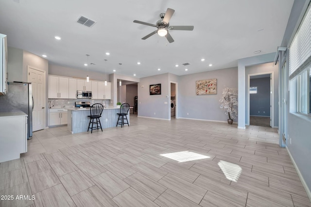 kitchen featuring a center island with sink, stainless steel appliances, light countertops, hanging light fixtures, and white cabinetry